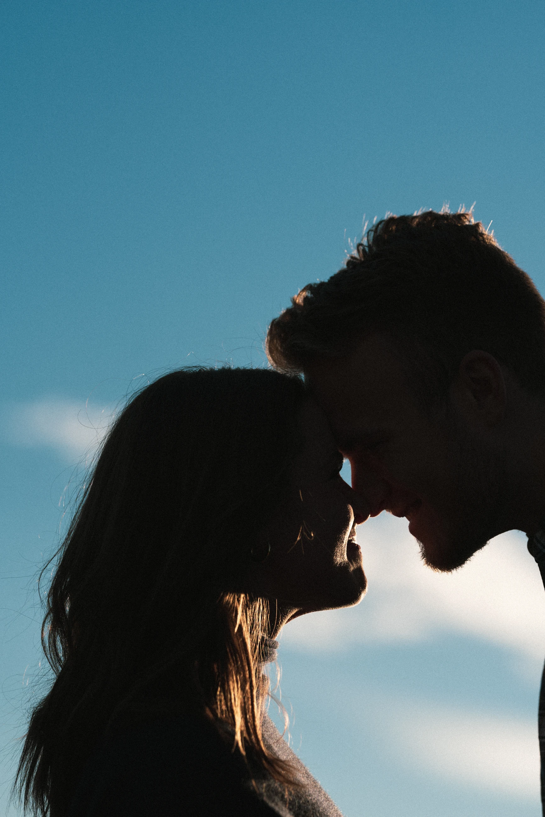 Couple touching foreheads in silhouette against a blue sky