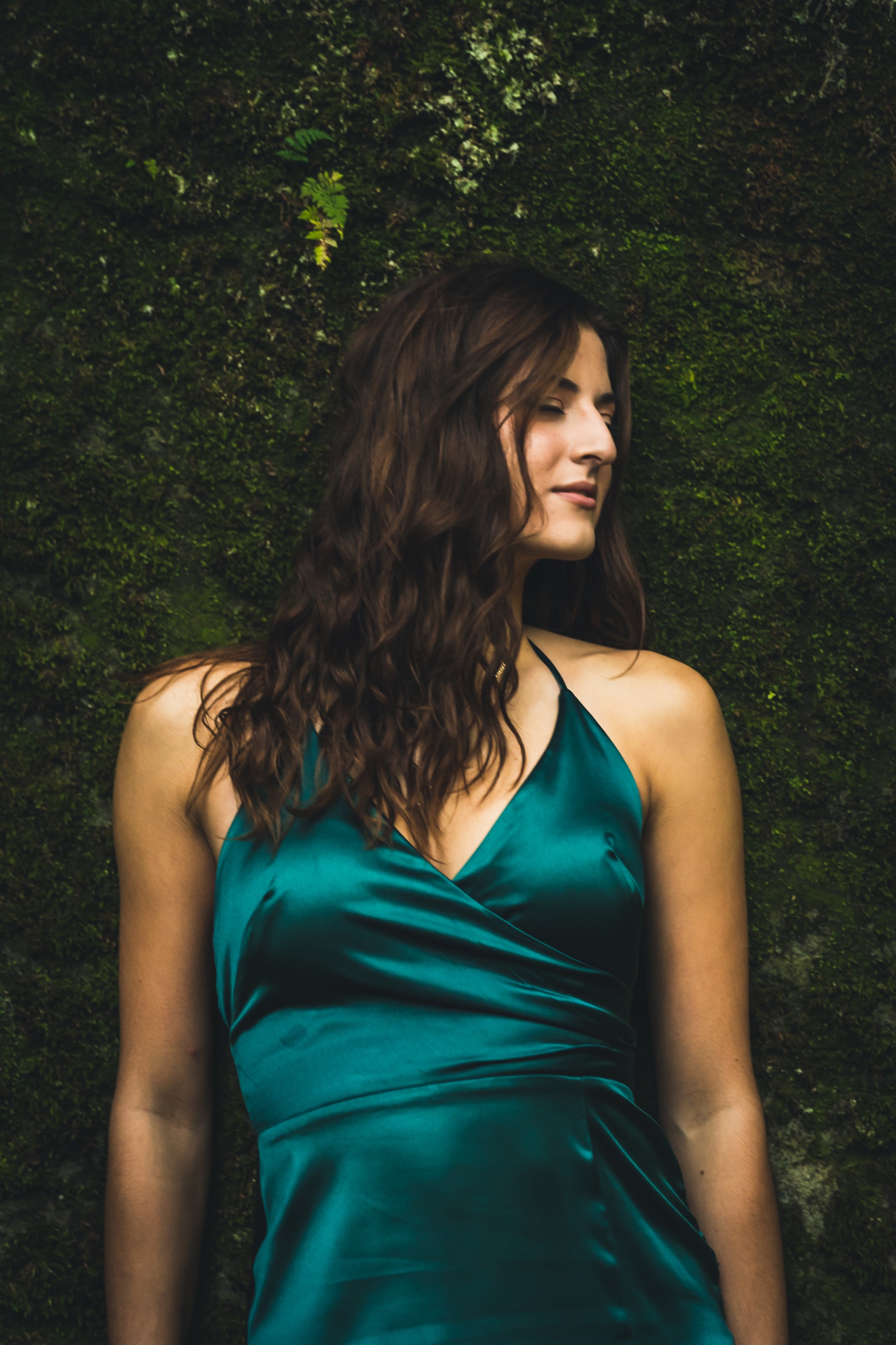 Senior in an emerald dress posed against a moss-covered wall
