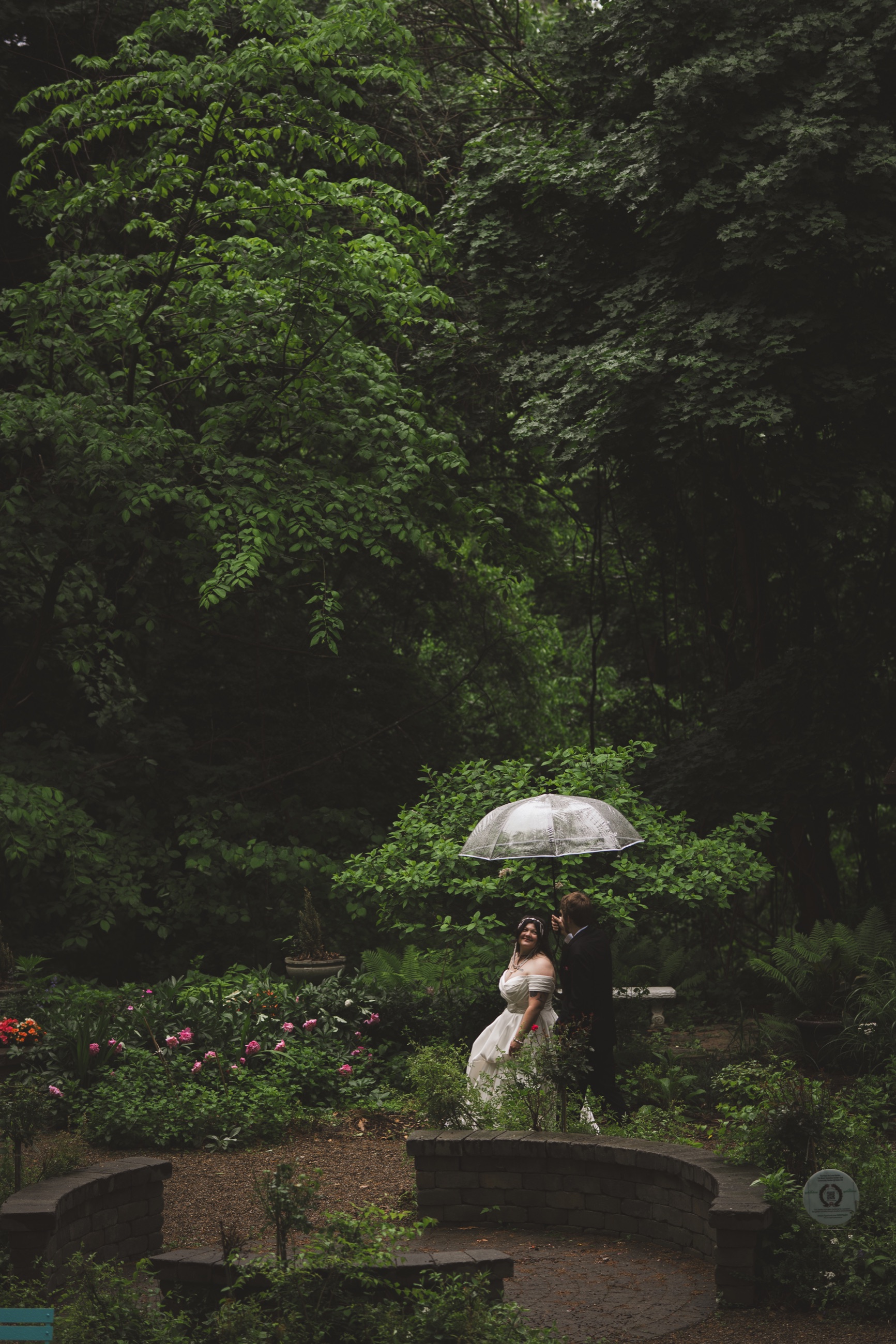 Newlyweds sharing an umbrella in a lush garden