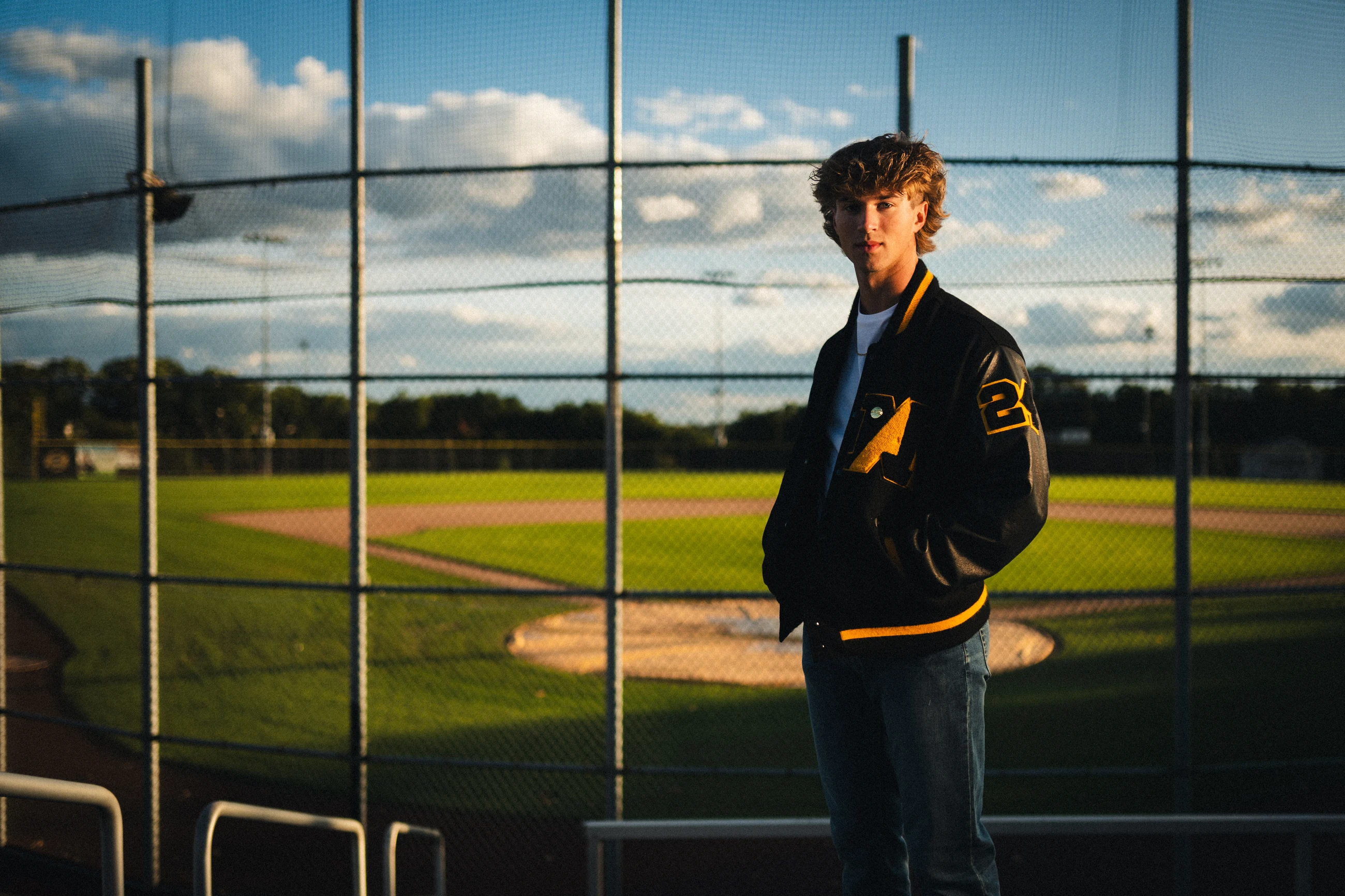 Senior standing at a baseball field under bright clouds