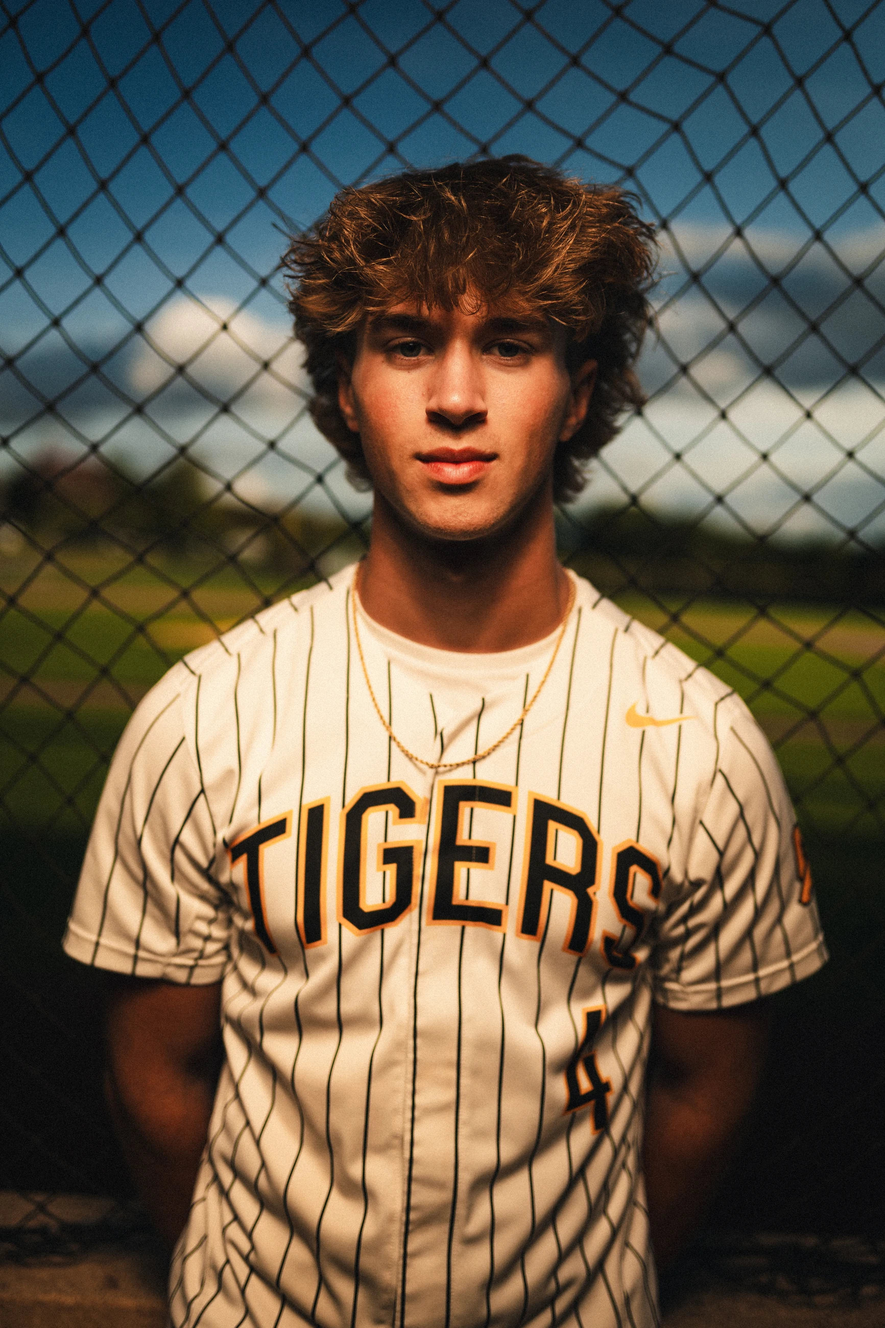 Senior baseball portrait framed by a chain-link fence