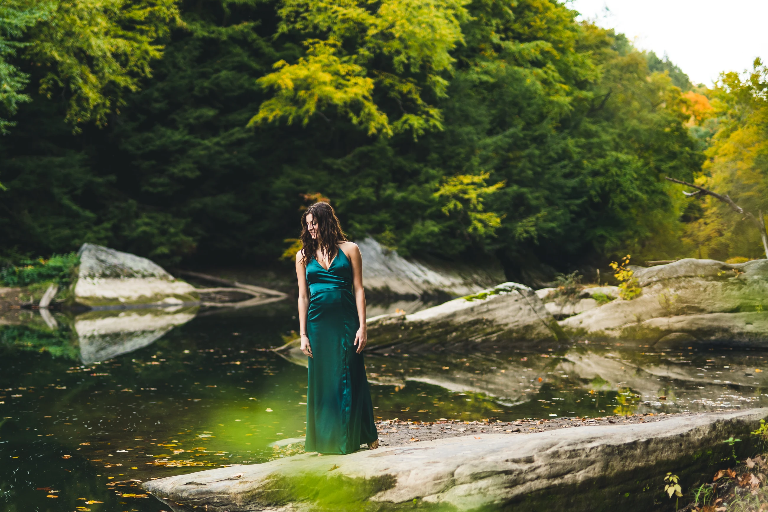 Senior in a green dress standing beside a rocky river